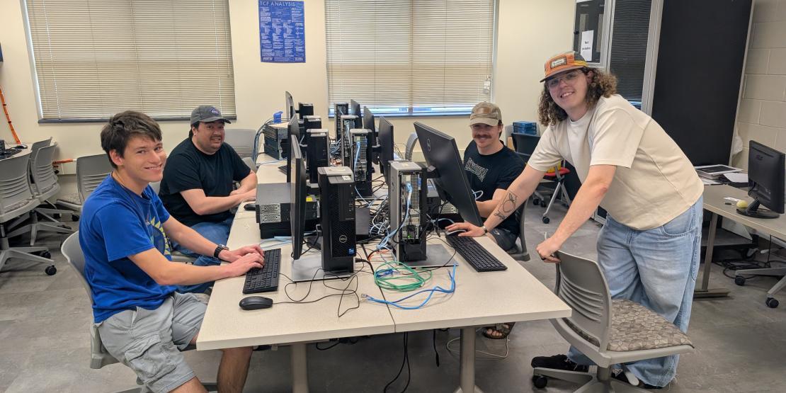 Four students stand around a desk with computers