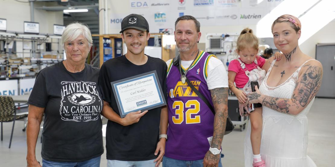 Carl Kidder stands with family and holding certificate