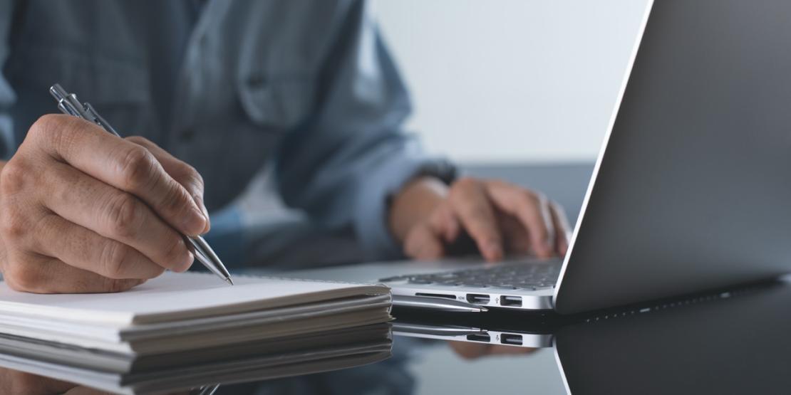 Person takes notes while working on a laptop.