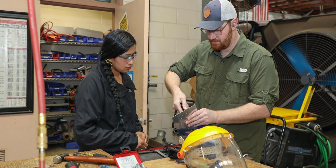 Instructor demonstrates metalworking techniques to an apprenticeship student in a workshop.
