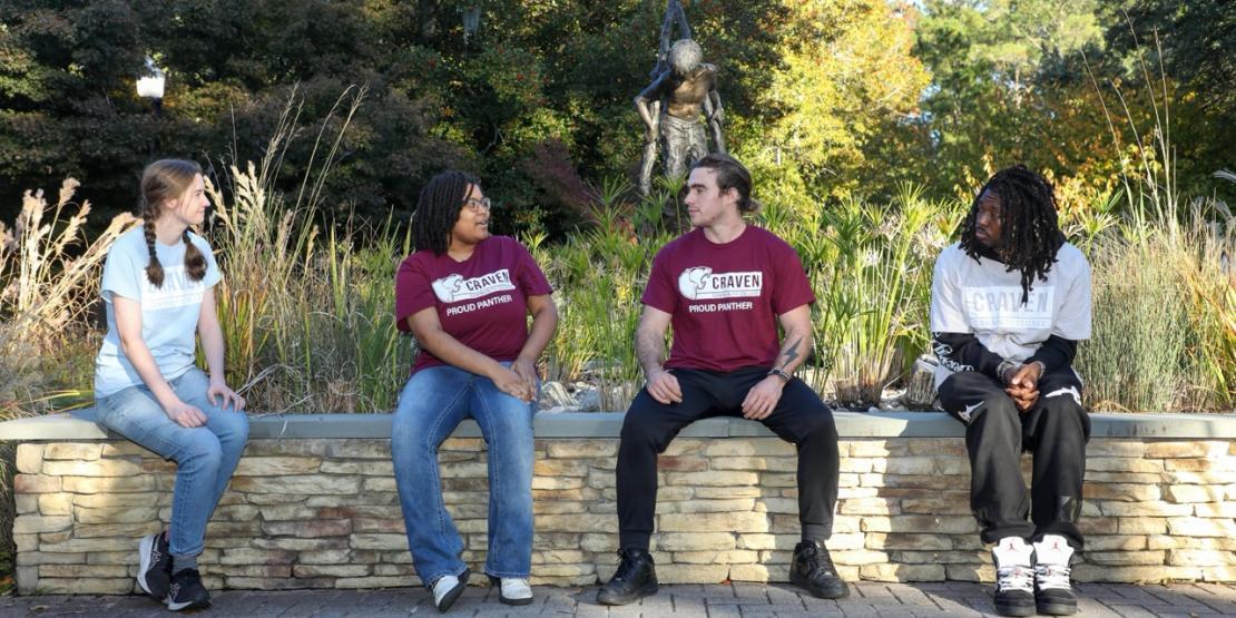 Four Craven Community College students sit together and talk in a landscaped area on campus.
