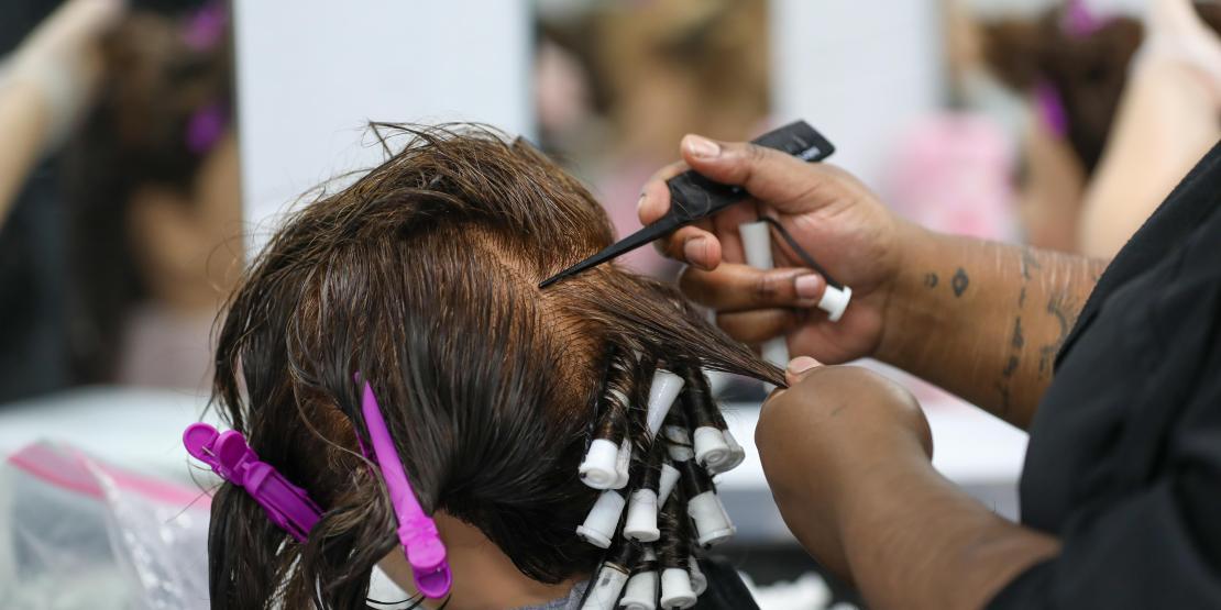Cosmetology student wraps sections of a mannequin’s hair around perm rods.