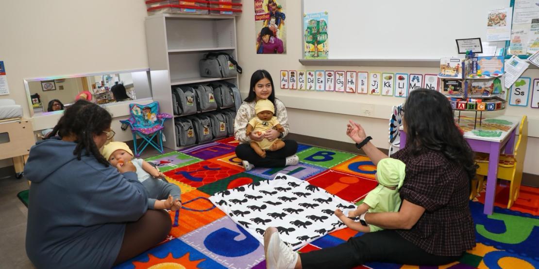 Early childhood education students practice infant care with baby dolls in a classroom.