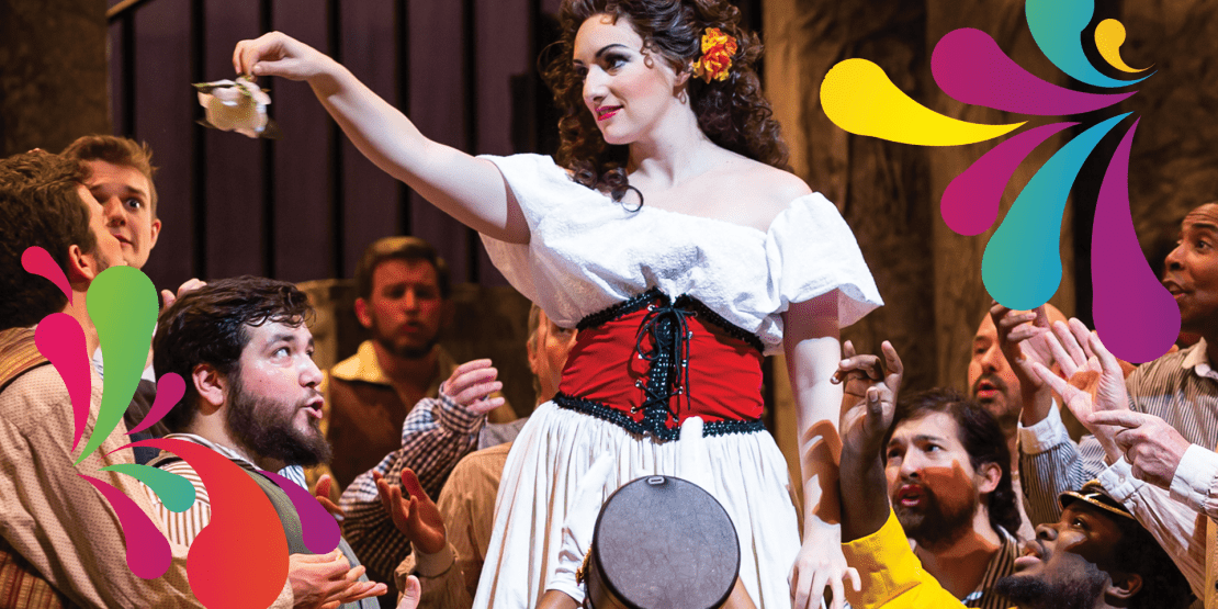 Carmen, dressed in a white blouse and red-and-black corset, dances above a crowd during a lively scene from Bizet’s Carmen, framed by colorful decorative flourishes.