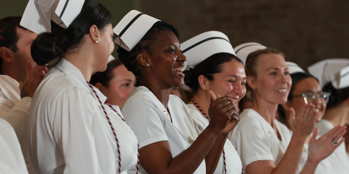 Nursing graduates in traditional white uniforms and caps celebrate during a pinning ceremony.