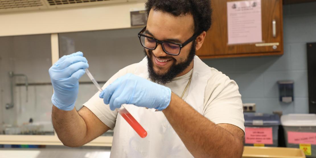 Science student uses a pipette to transfer liquid into a test tube during a laboratory experiment.
