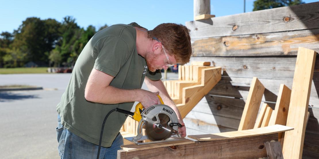 Construction student wearing safety glasses uses a circular saw to cut lumber during hands-on training.