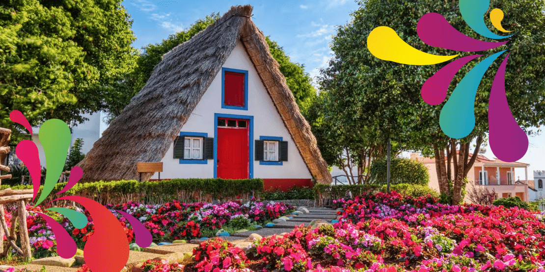 Traditional thatched-roof cottage with red-trimmed windows and doors surrounded by colorful flower gardens.