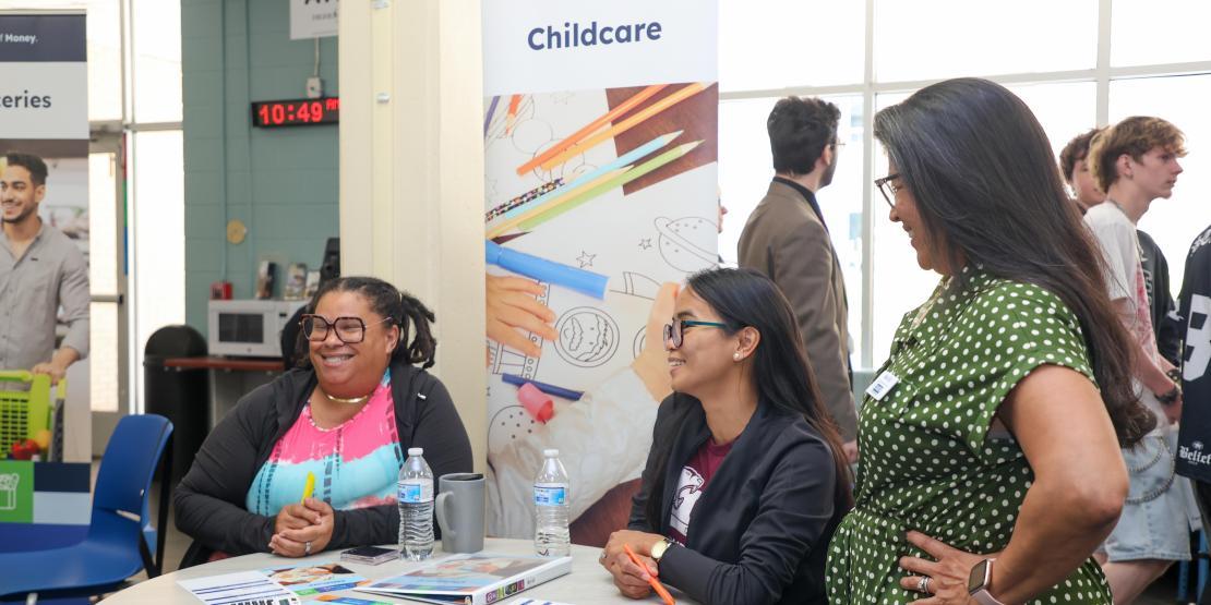 Three females infront of a childcare banner and smiling