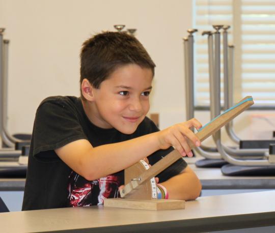 Young boy sits at desk with rubber band cannon
