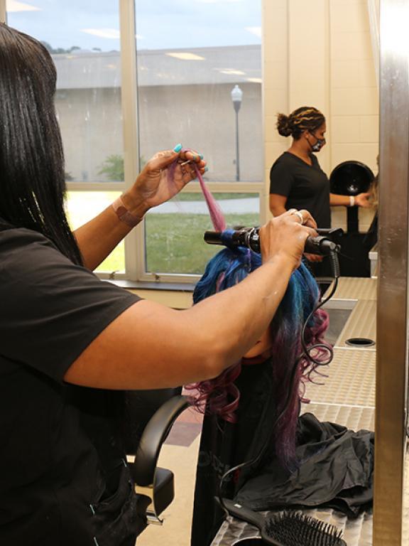 cosmetology student practices curling hair on wig