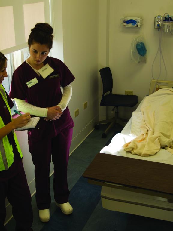 Two nurses practice caring for patient in bed