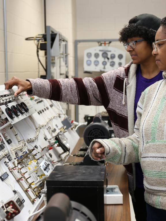 Two aviation systems technology students in a classroom look over small plane controls