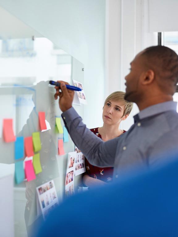 Three colleagues work together on business strategy while writing on whiteboard with colorful sticky notes
