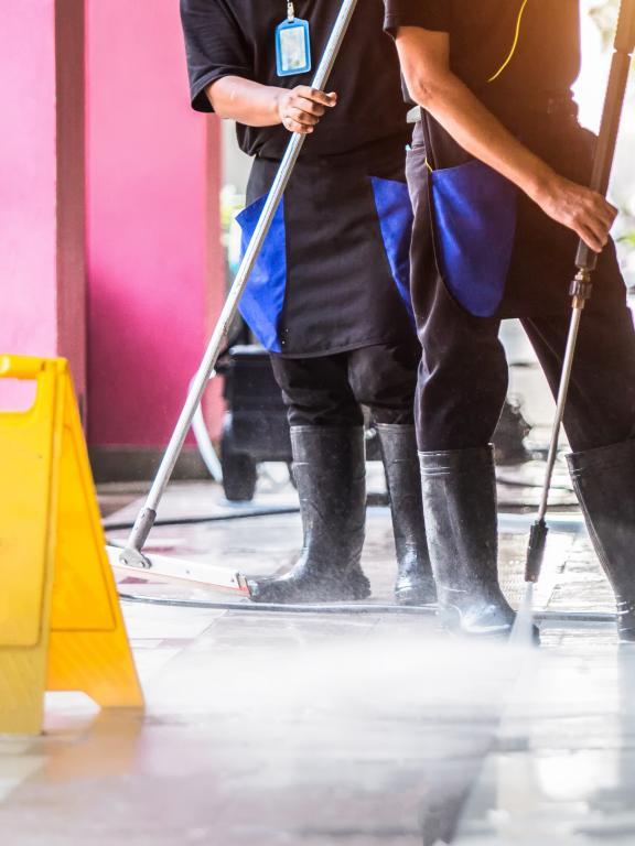 two people in rain boots power wash a concrete floor