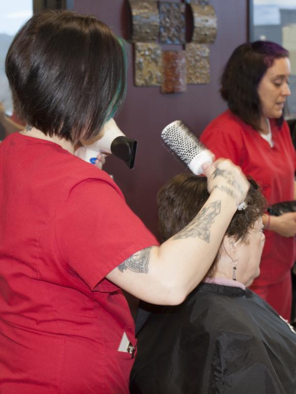 Cosmetology student blow dries and brushes a client's hair