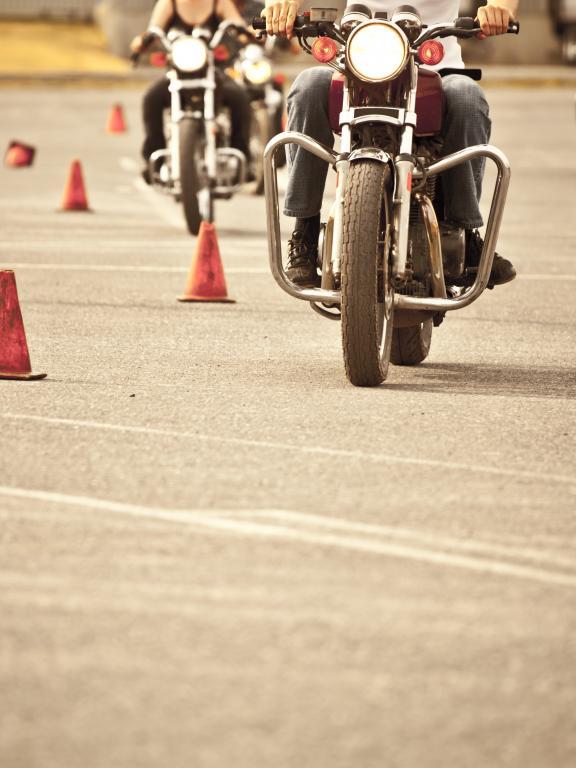 Three people riding motorcycles through cones in parking lot