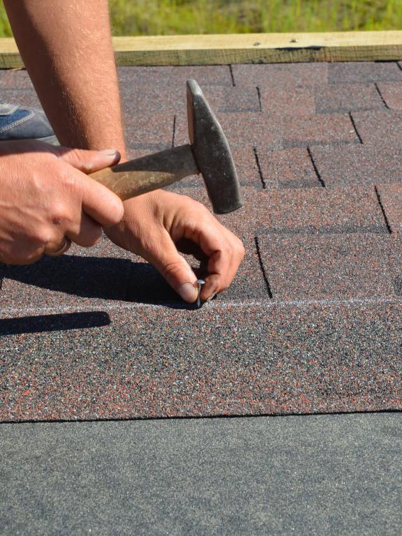 Person hammers nail into roof shingles