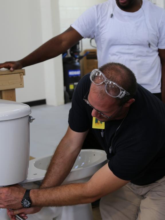 Man demonstrates plumbing procedures on model toilet