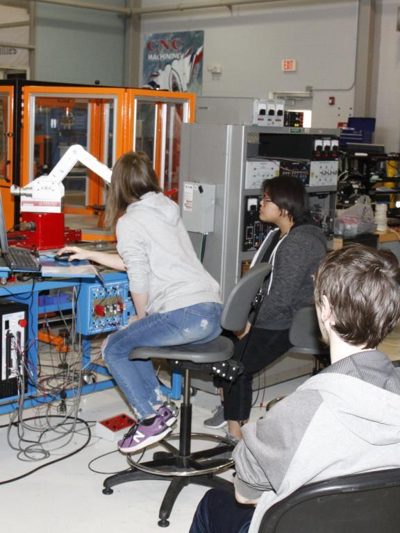 A group of students watch as female student operates machinery