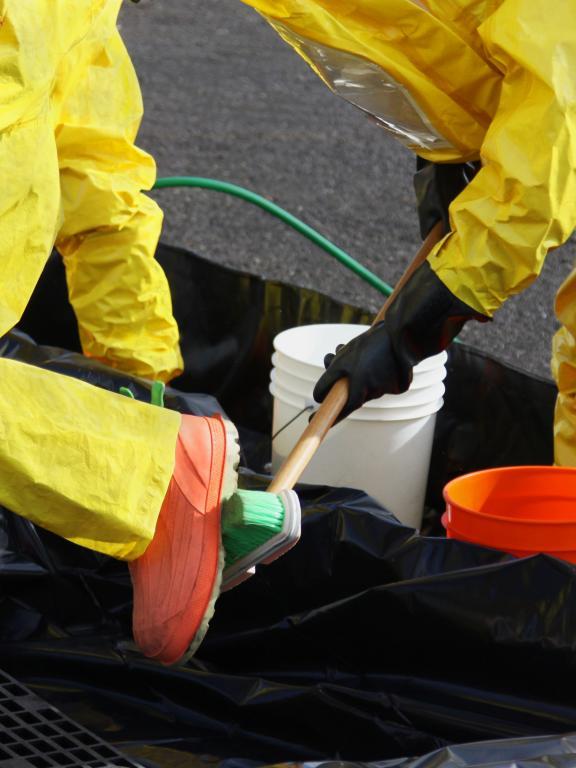 Person in yellow hazmat suit scrubs the bottom of another person's foot