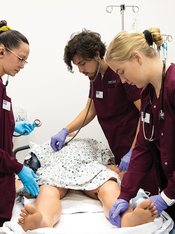 Three nursing students practice on a simulated patient