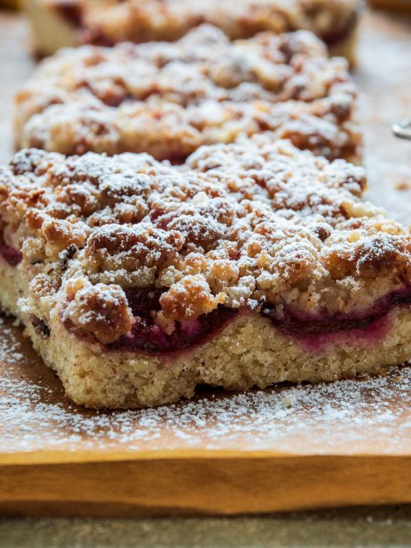 Moist, delectable crumb cake squares on wooden baking surface with flour sifter and mixing bowl