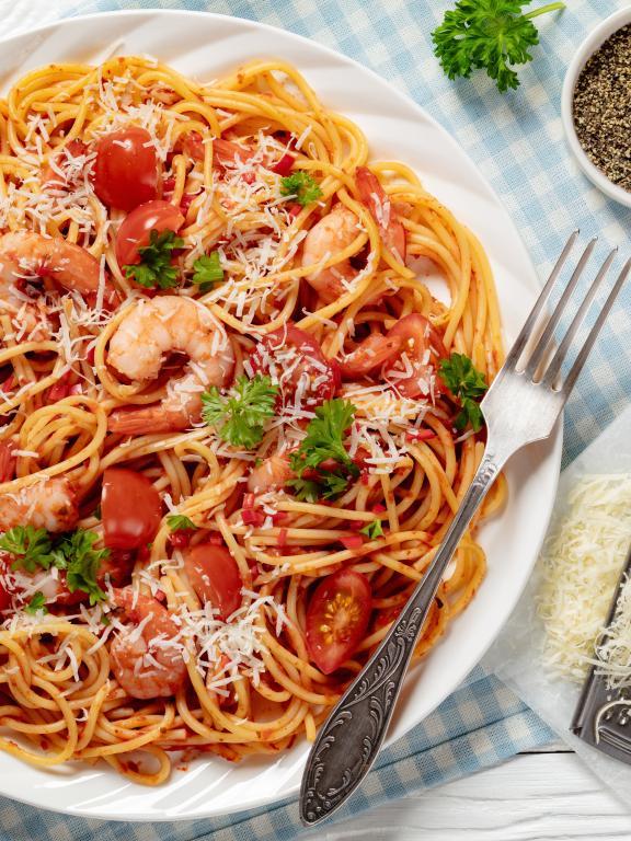 Shrimp fra diavolo on white plate with metal decorative fork, small white bowl of spices, and grater with parmesan cheese