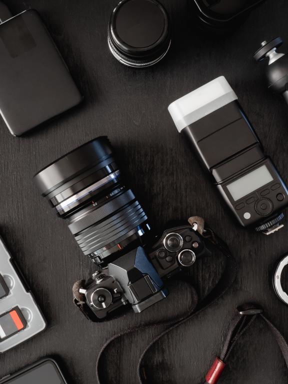 top view of work space photographer with digital camera, flash, cleaning kit, memory card, external harddisk, USB card reader, laptop and camera accessory on black table background.