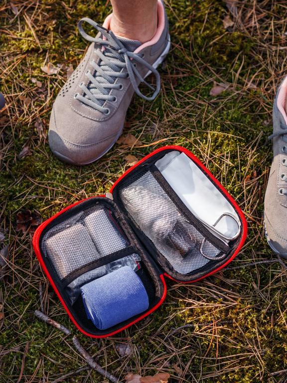 Close up of person in tennis shoes standing in grass next to an open first aid kit and backpack