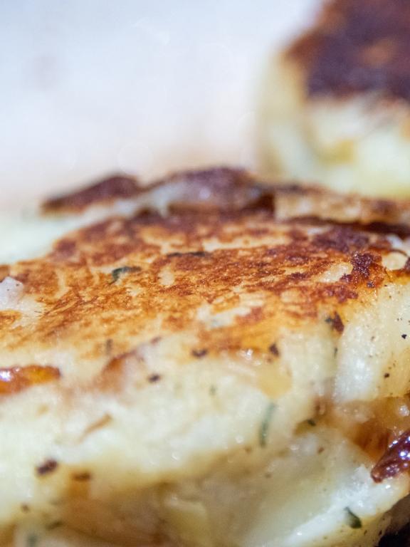 A single uncooked round salt cod fishcake prepared for frying. The mixture of savory, potato, salt codfish, and butter is shaped into a small patty as a dish once fried in butter and browned goldenly