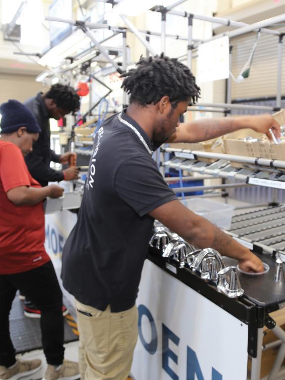 Two males and one female student work on a mock assembly line