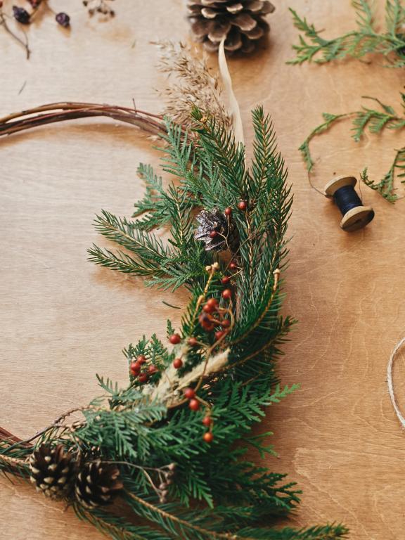 Holiday wreath craft with foliage, pinecones, string and scissors