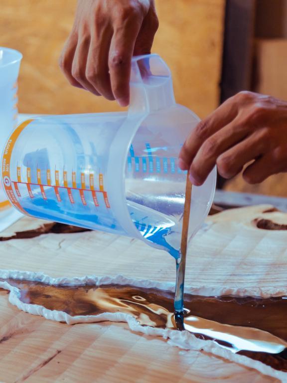 Person pouring liquid epoxy into abstract pattern on a wooden table