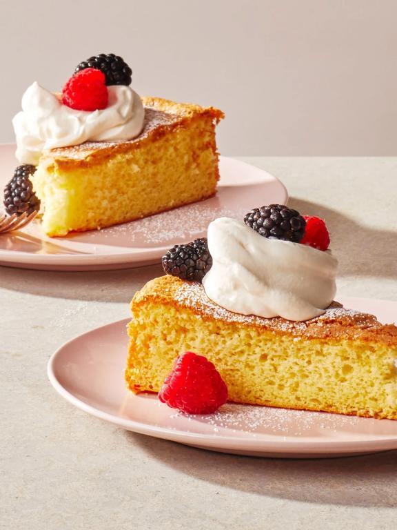 Two slices of Génoise cake on pastel pink plates, topped with a dollop of whipped cream, blackberries, and raspberries