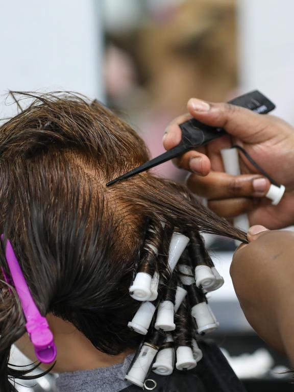 Cosmetology student wraps sections of a mannequin’s hair around perm rods.