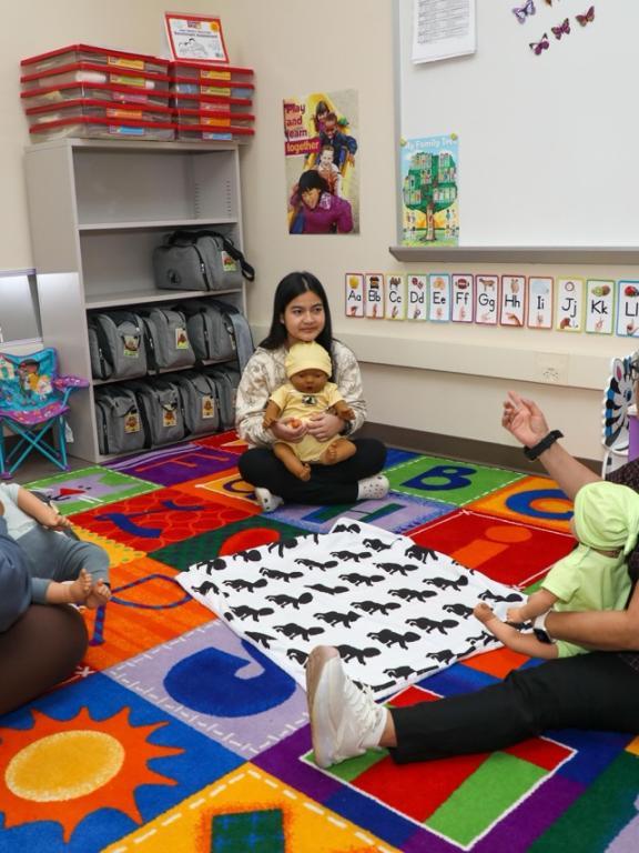 Early childhood education students practice infant care with baby dolls in a classroom.