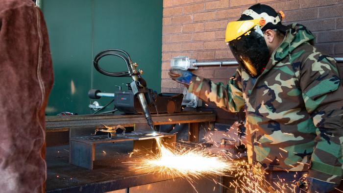 Two welding students practice welding outside