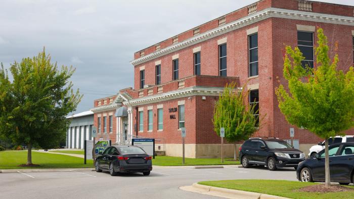 Exterior of Taylor Hall at Craven Community College’s Volt Center, a three-story red brick building surrounded by trees and a campus parking area.