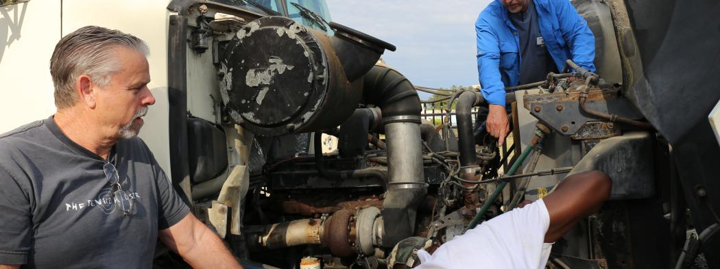 Diesel systems student works on engine outside with two instructors