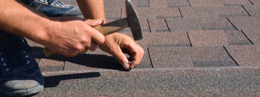 Person hammers nail into roof shingles