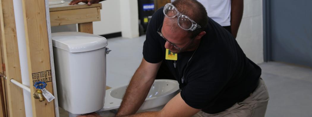Man demonstrates plumbing procedures on model toilet