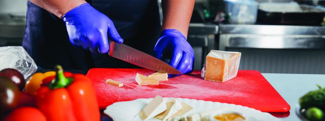 Chef in blue gloves slices cheese on red cutting board