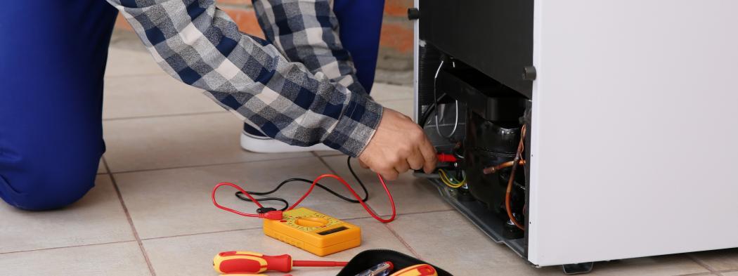 Male home appliance technician using multimeter and repairing broken refrigerator indoors