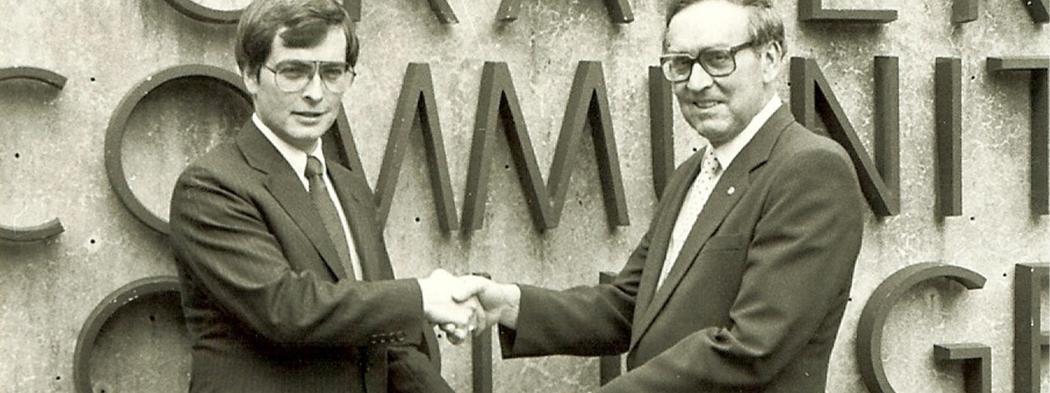 Craven CC's founding president, Dr. Thurman Brock, shakes a man's hand and accepts a check in front of the Craven sign in the 1960s