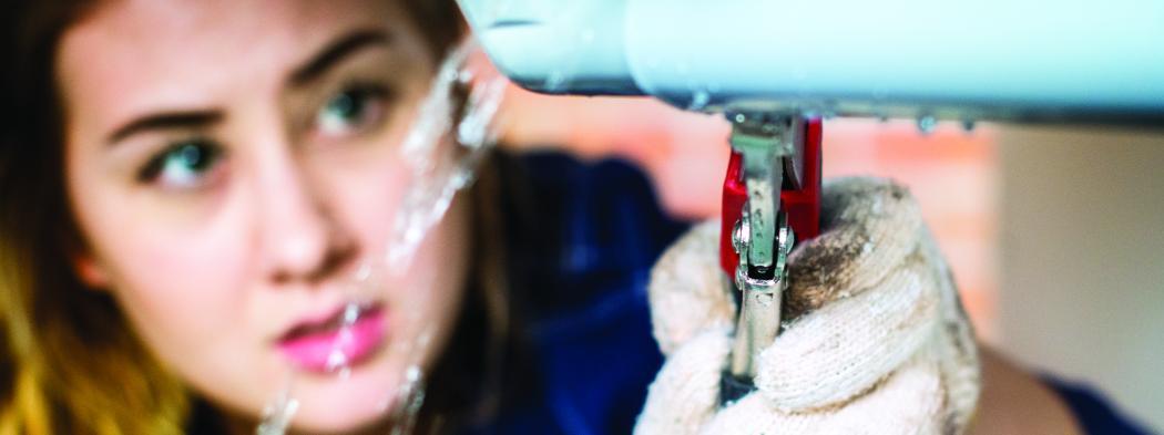 Female plumber tightens pipe that is leaking