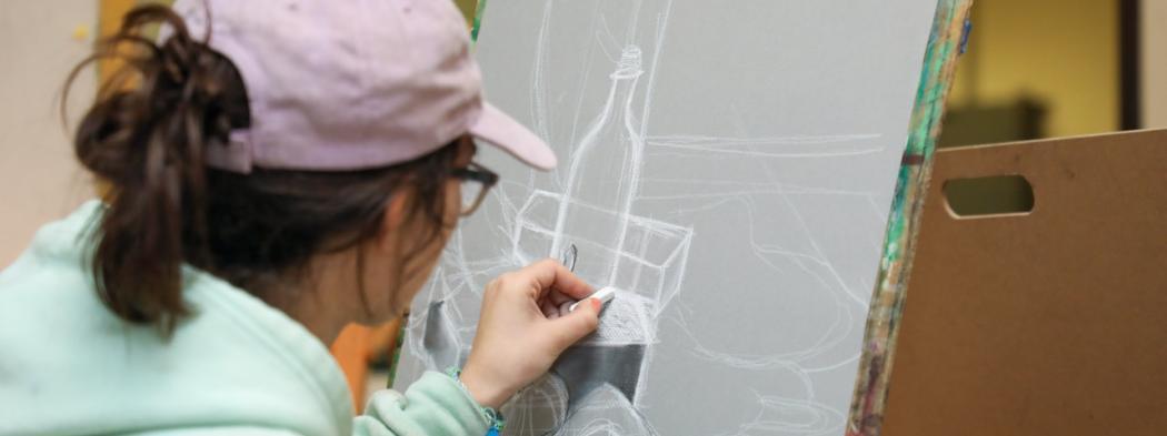 Student drawing a still life with white chalk on gray paper during an art class.