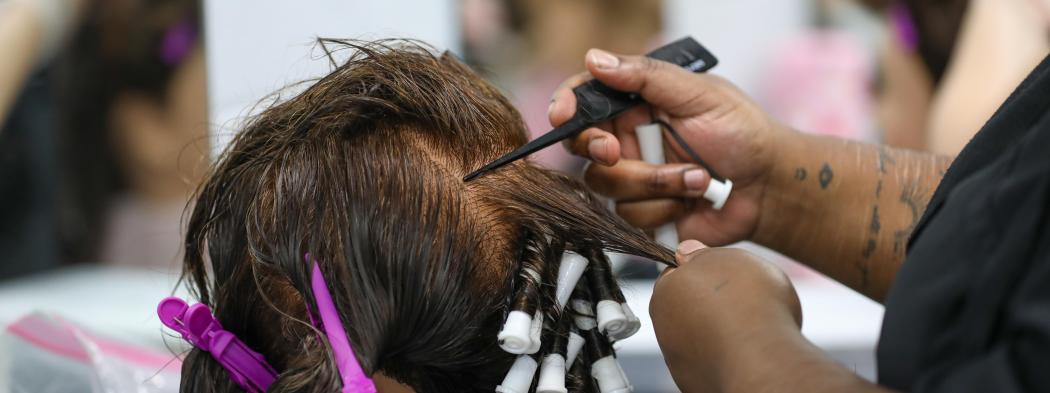 Cosmetology student wraps sections of a mannequin’s hair around perm rods.