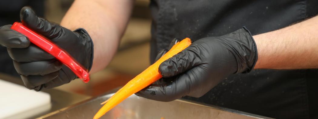Culinary student wearing gloves peels a carrot during food preparation.