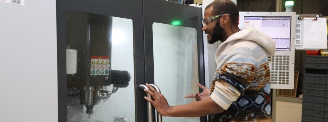 Manufacturing student wearing safety glasses operates a CNC milling machine.